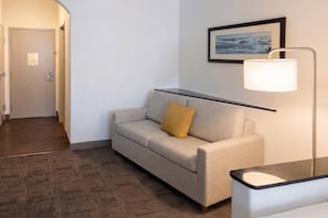 A hotel room with a sofa, a lamp, a framed picture on the wall, and a wooden floor. - Comfort Suites Galveston Cruise Port Area – Beachside (Galveston)