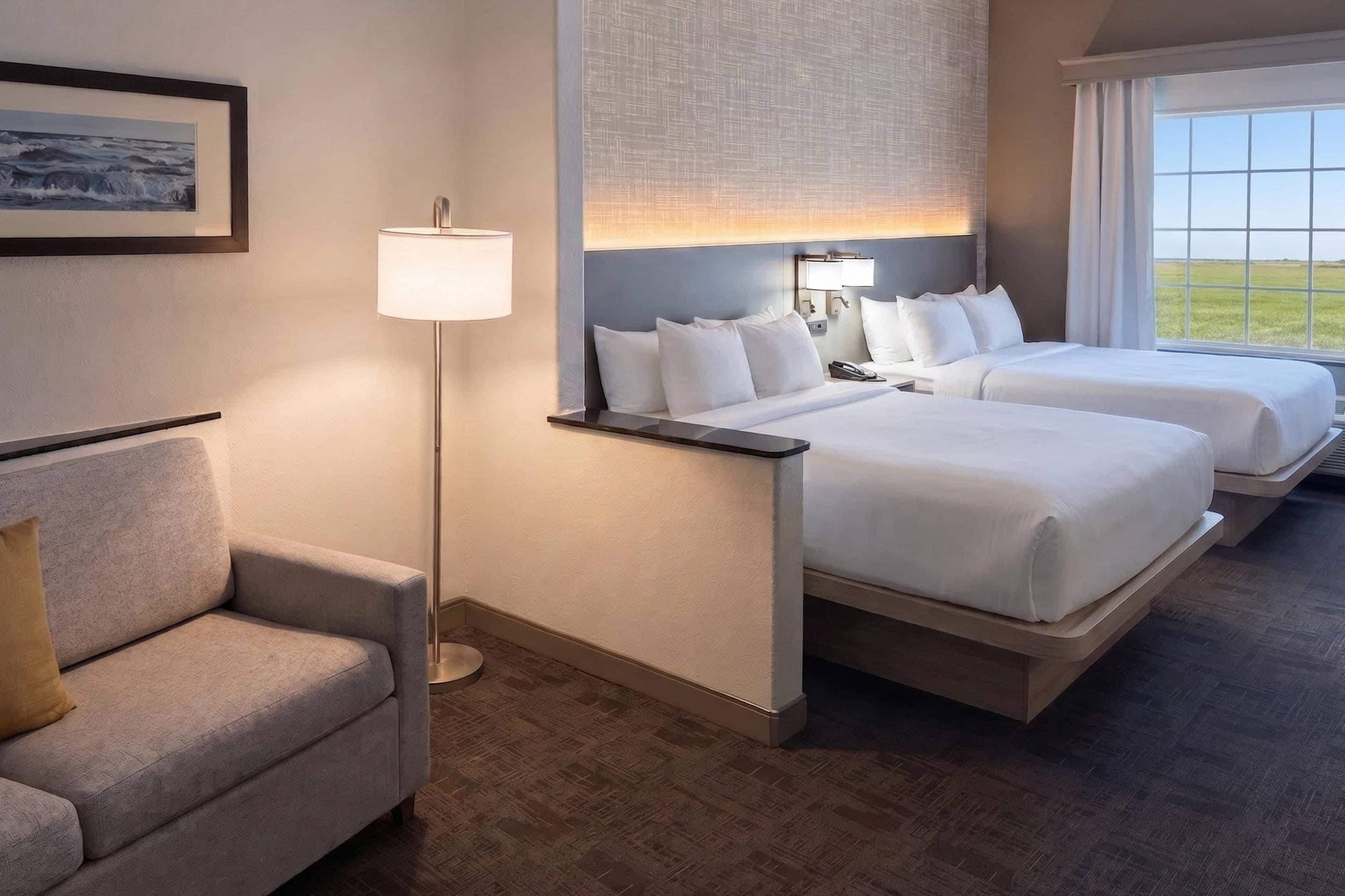 A hotel room with two beds, a sofa, a floor lamp, and a window with a view.