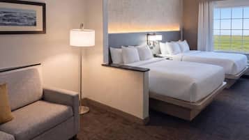 A hotel room with two beds, a sofa, a floor lamp, and a window with a view.
