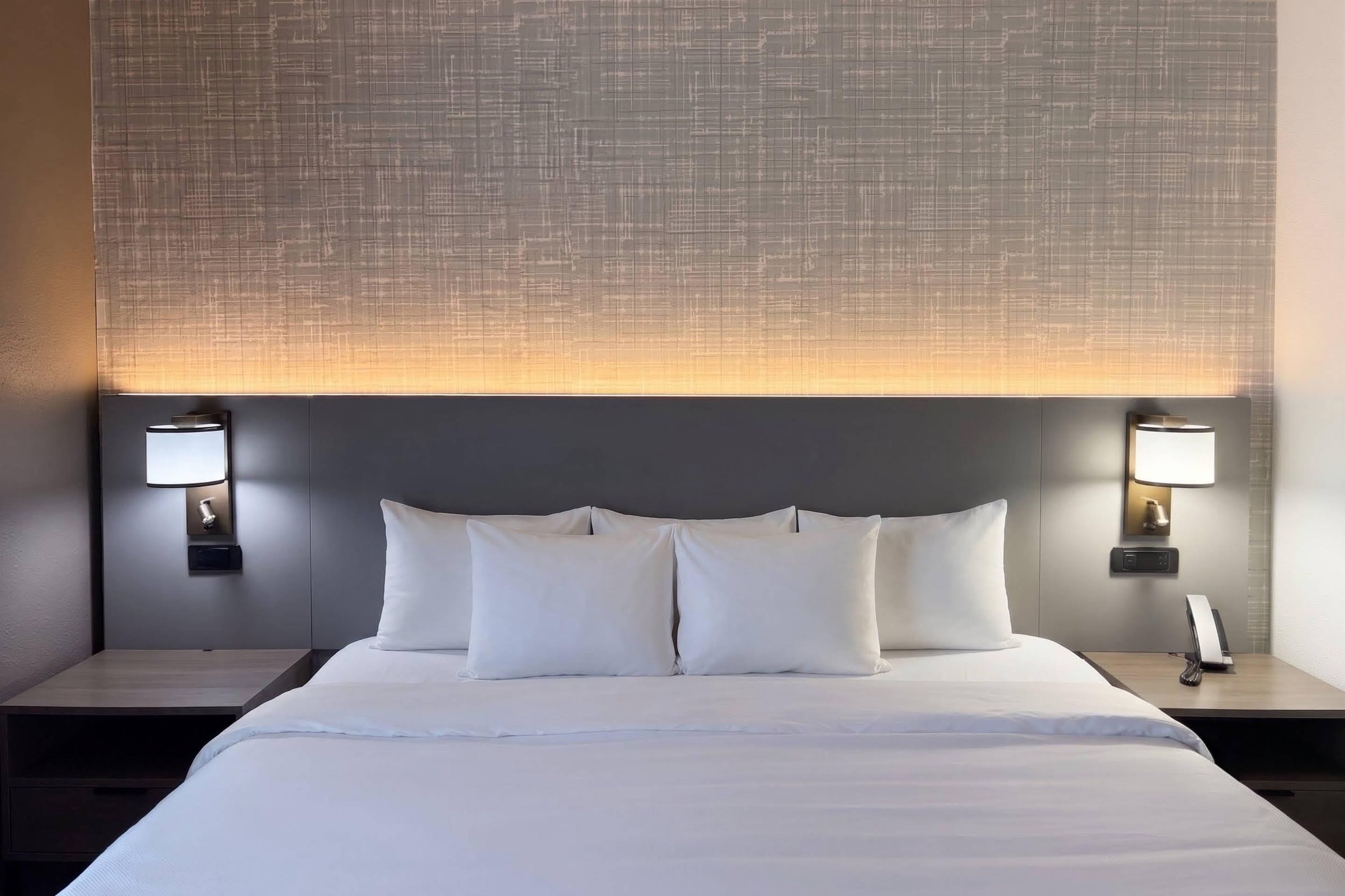 Een hotelkamer met een groot bed, twee nachtkastjes en een hoofdbord met een geribbeld patroon.