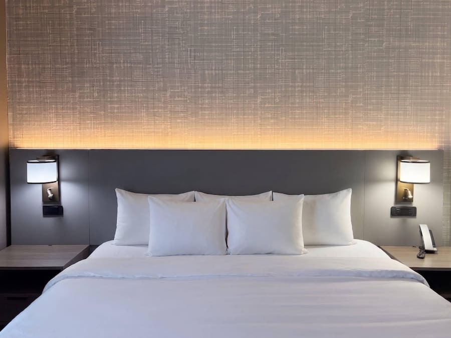Una habitación de hotel con una cama grande, dos mesitas de noche y un cabecero con textura.
