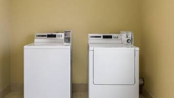 Twee witte wasmachines met een frontpaneel in een hoek, met beige wanden en betegelde vloer.