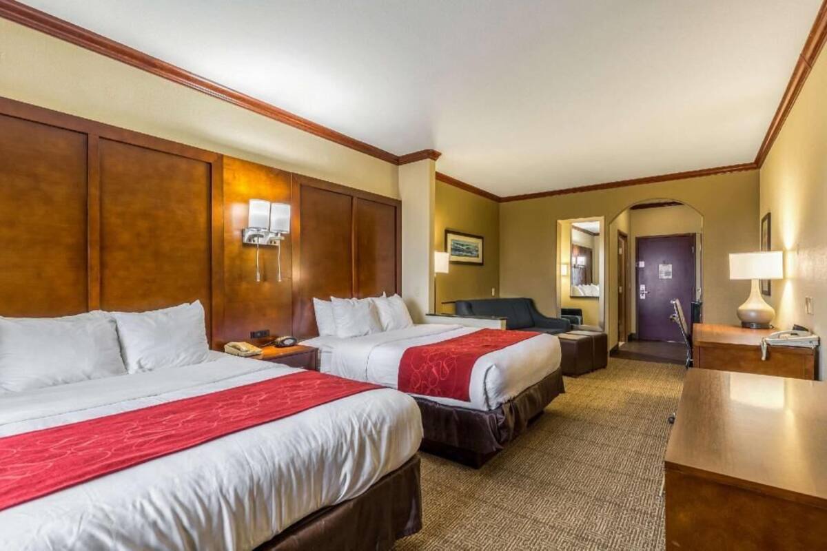 Una habitación de hotel con dos camas, un escritorio, una silla, una lámpara y una puerta.