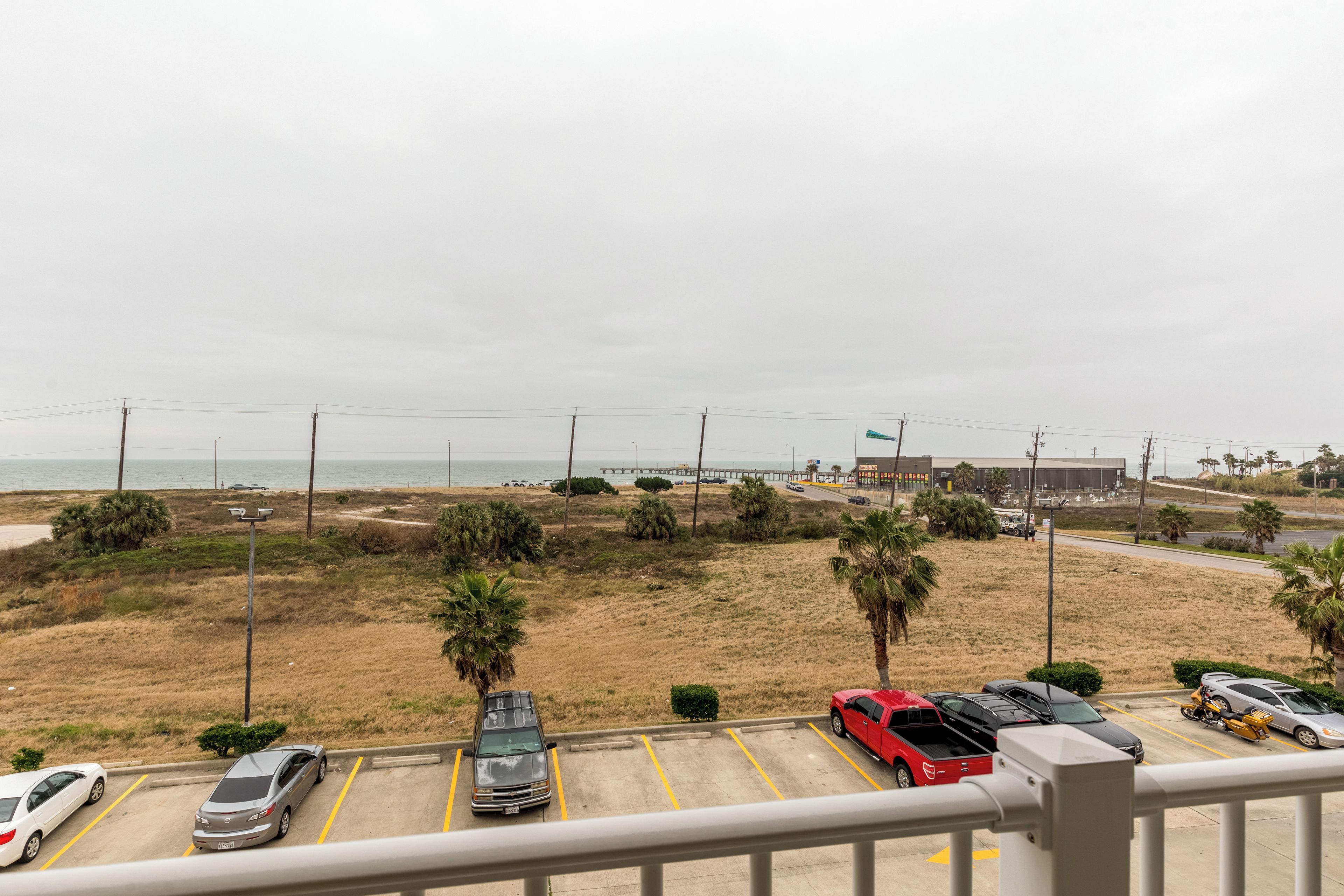 Um estacionamento com vários carros, um edifício ao fundo e vista para a praia.