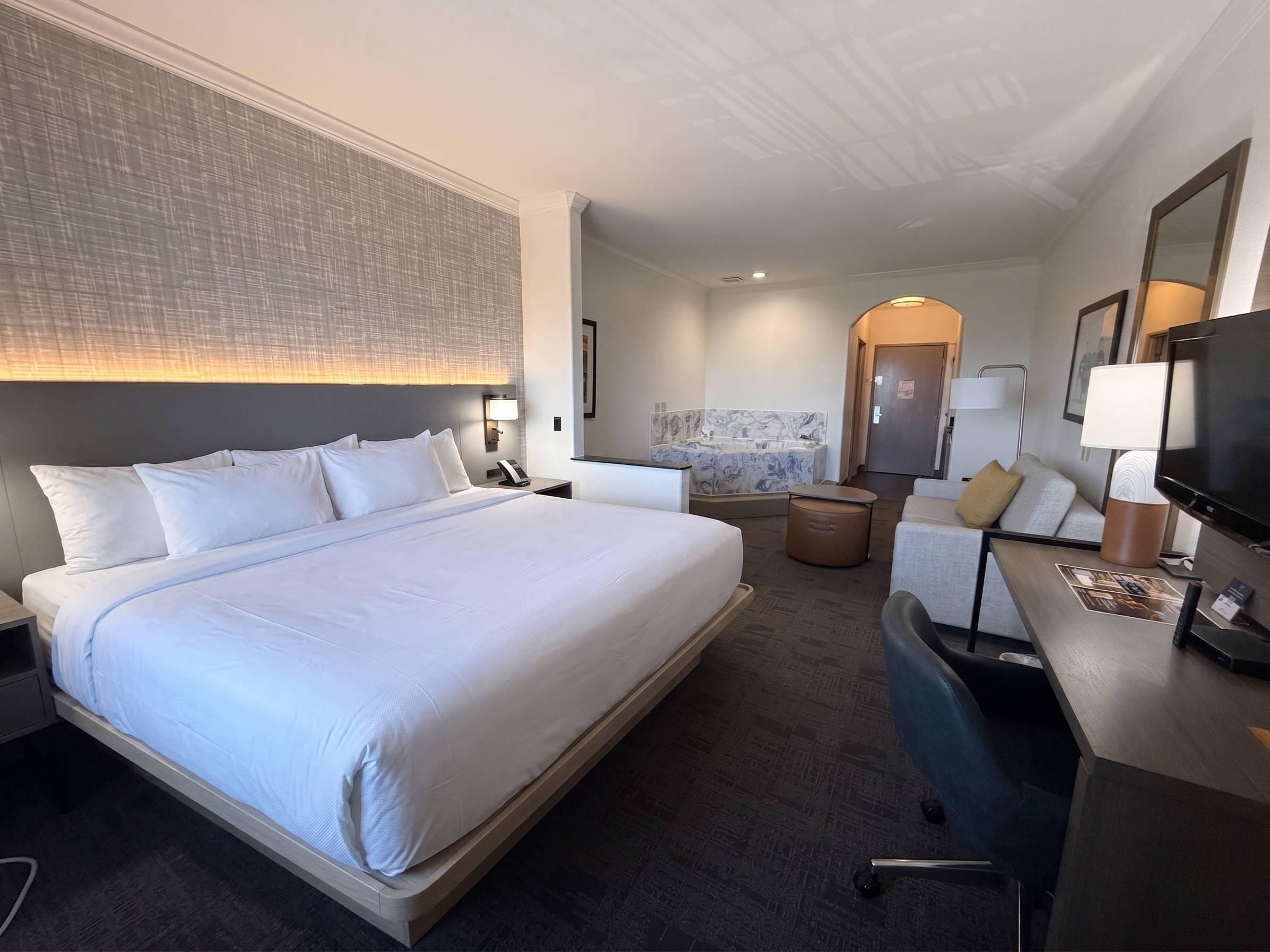 A hotel room with a large bed, a desk with a chair, a sofa, a bathroom with a marble sink, and a television.