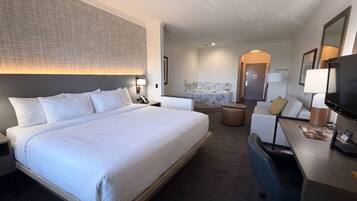 A hotel room with a large bed, a desk with a chair, a sofa, a bathroom with a marble sink, and a television.