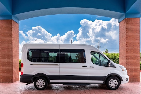 Una camioneta blanca estacionada bajo una estructura azul, con un cielo despejado y nubes al fondo.