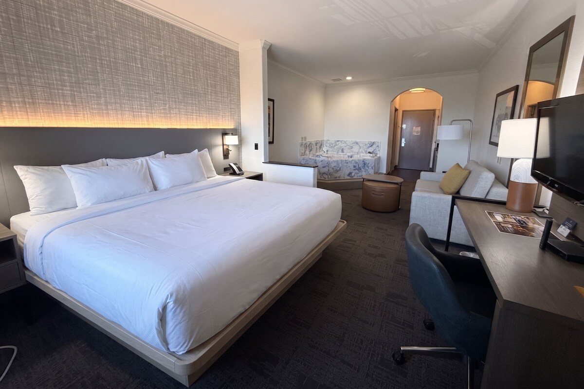 Habitación de hotel con una cama grande, un escritorio con una silla, un baño con lavamanos de mármol y un televisor.