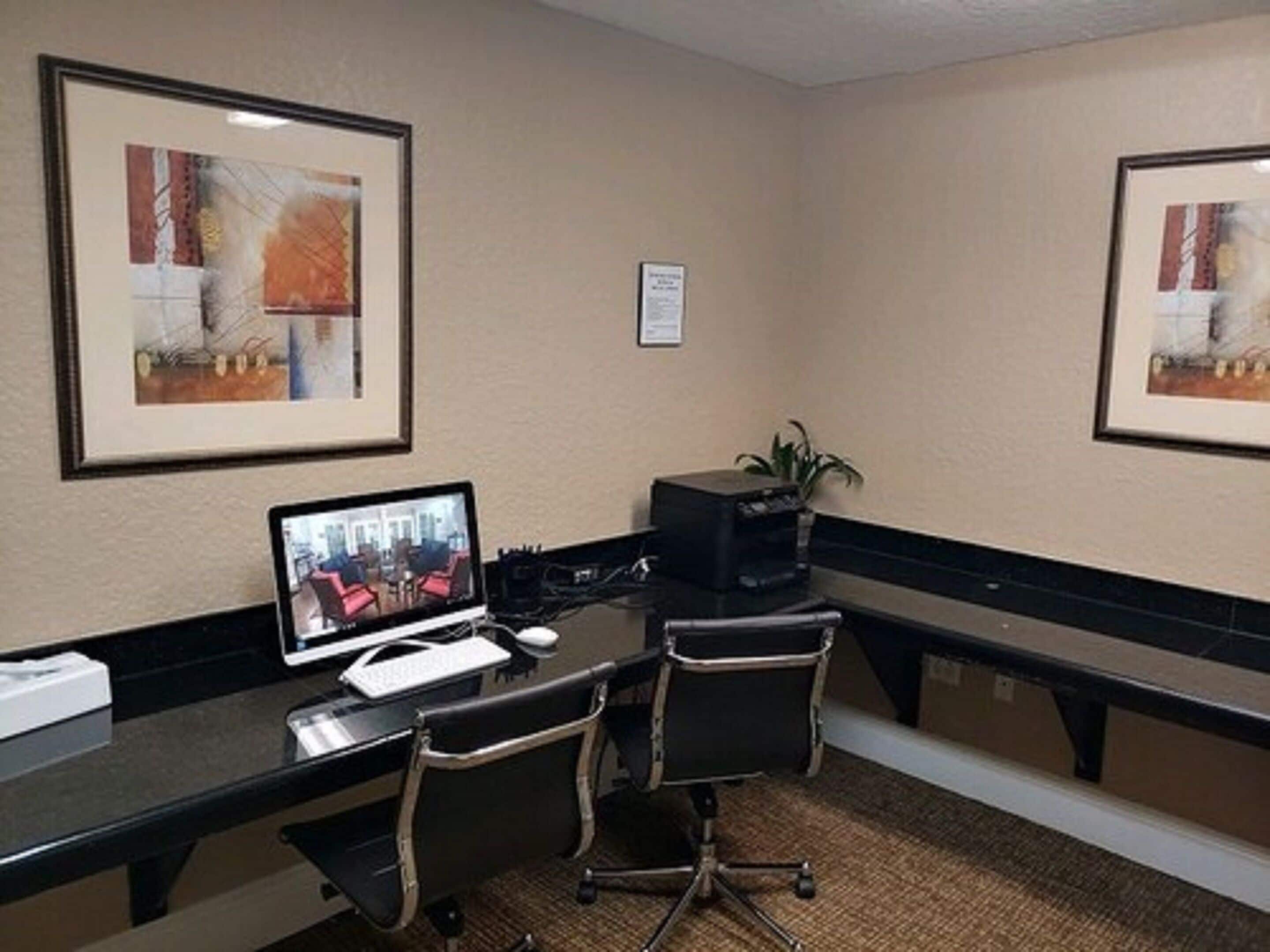 A conference room with a desk, two chairs, a computer, and framed artwork on the walls.