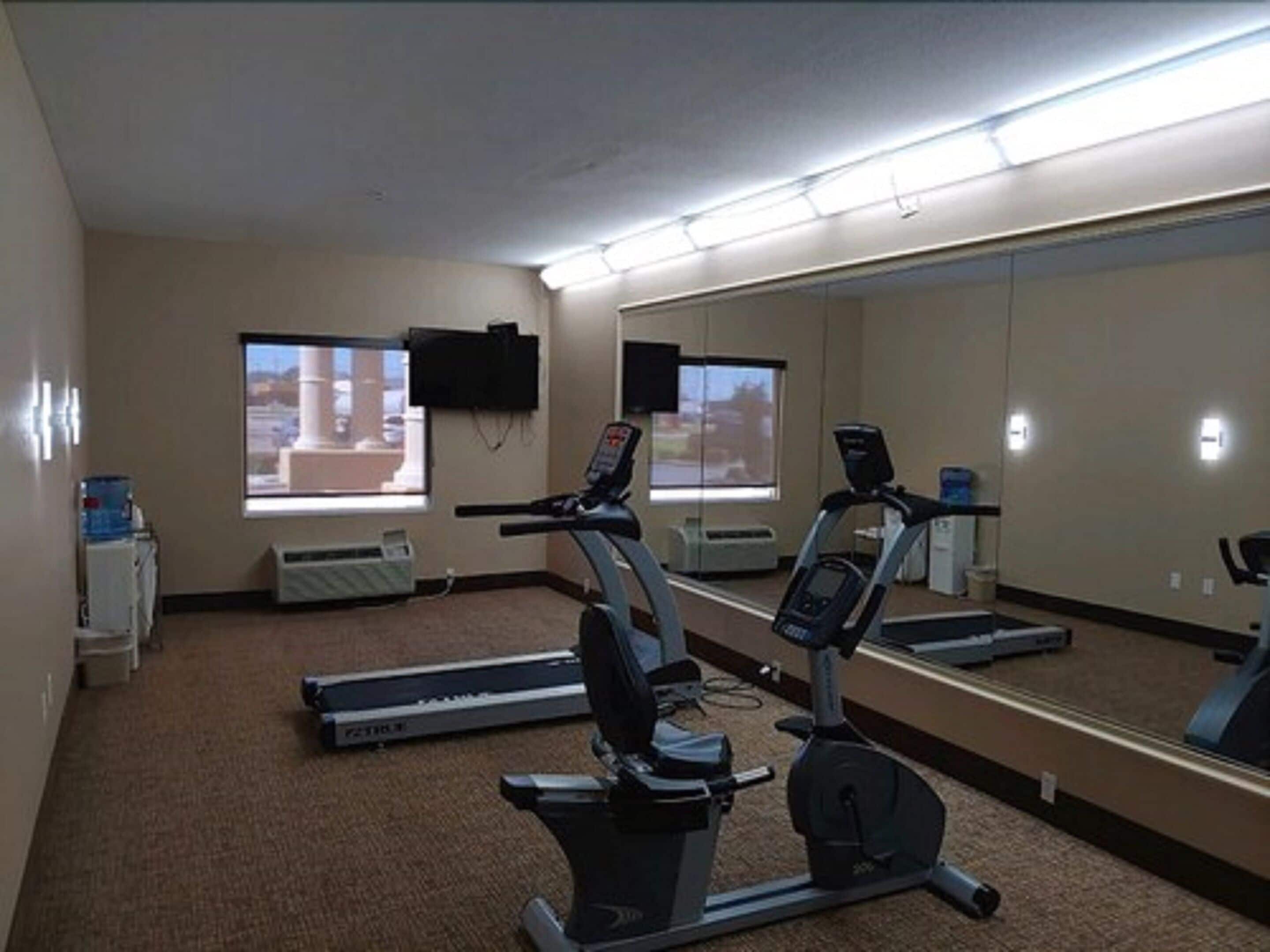 A gym with treadmills, an elliptical, and a stationary bike. There are windows with views of buildings outside.