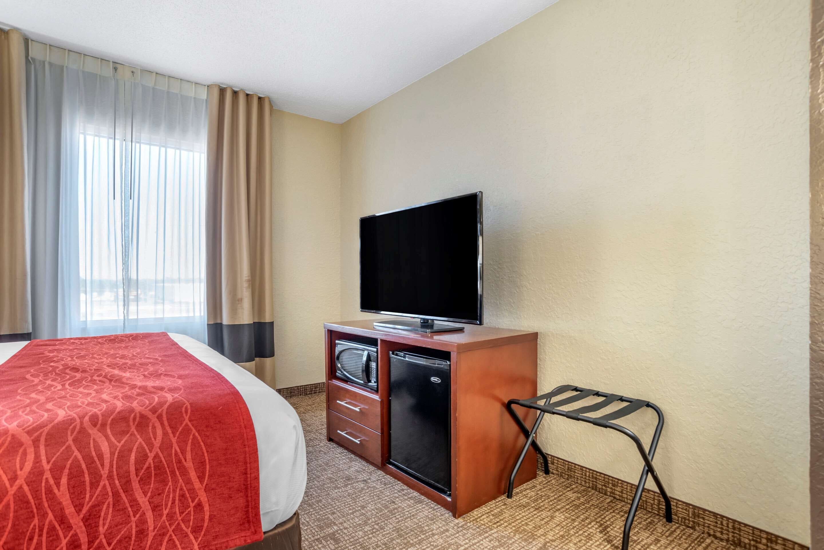 A hotel room with a bed, a television on a wooden cabinet, a small refrigerator, and a chair.