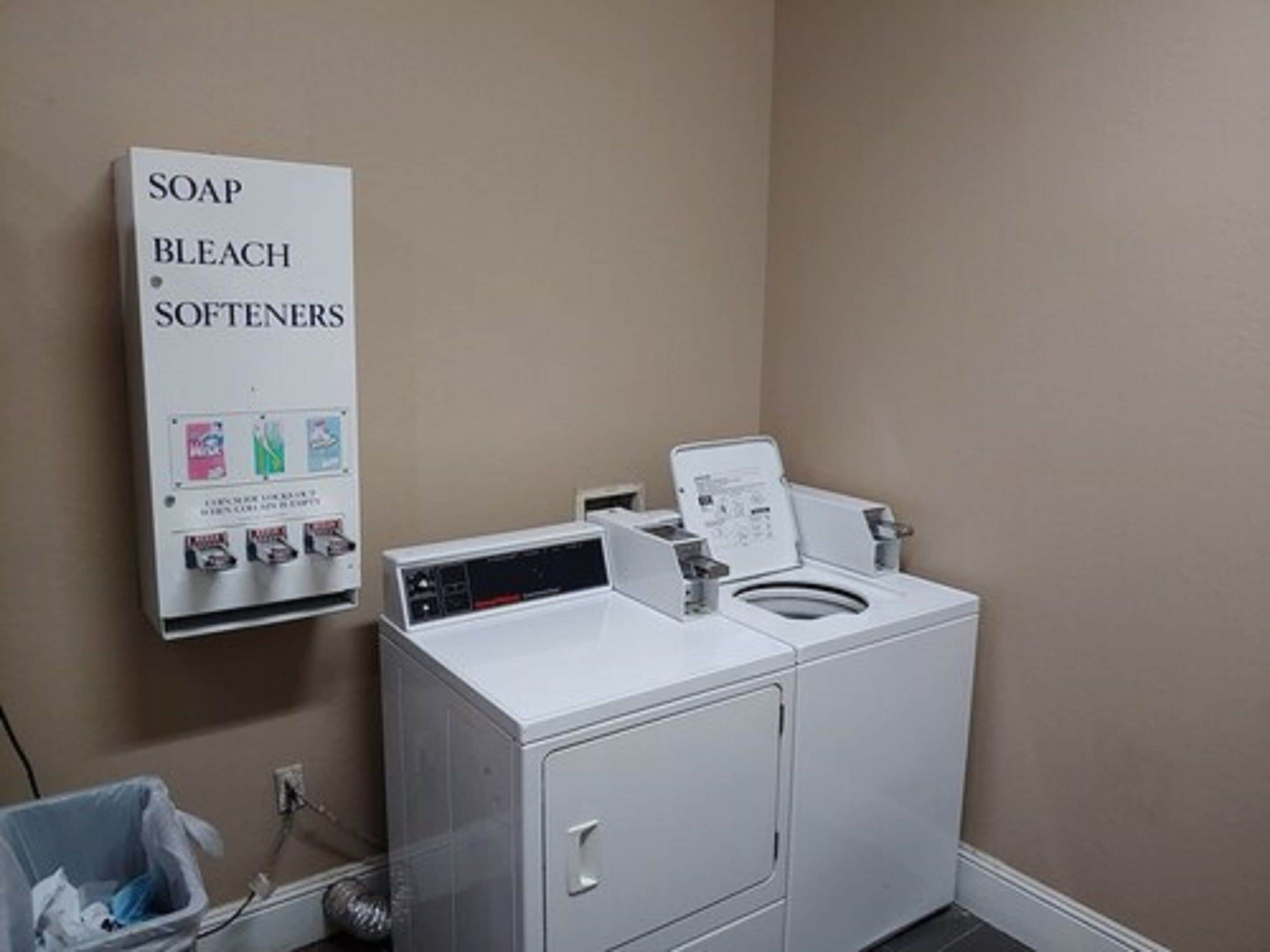 A laundry area with a washing machine, a detergent dispenser, and a trash bin.