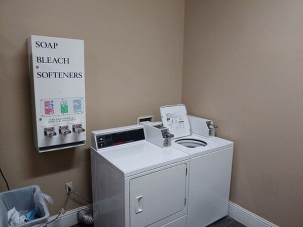 A laundry area with a washing machine, a detergent dispenser, and a trash bin. - Comfort Inn & Suites Marianna I-10 (Marianna)
