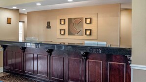 Un área de recepción con un mostrador de madera oscura, un reloj grande montado en la pared y diplomas enmarcados.