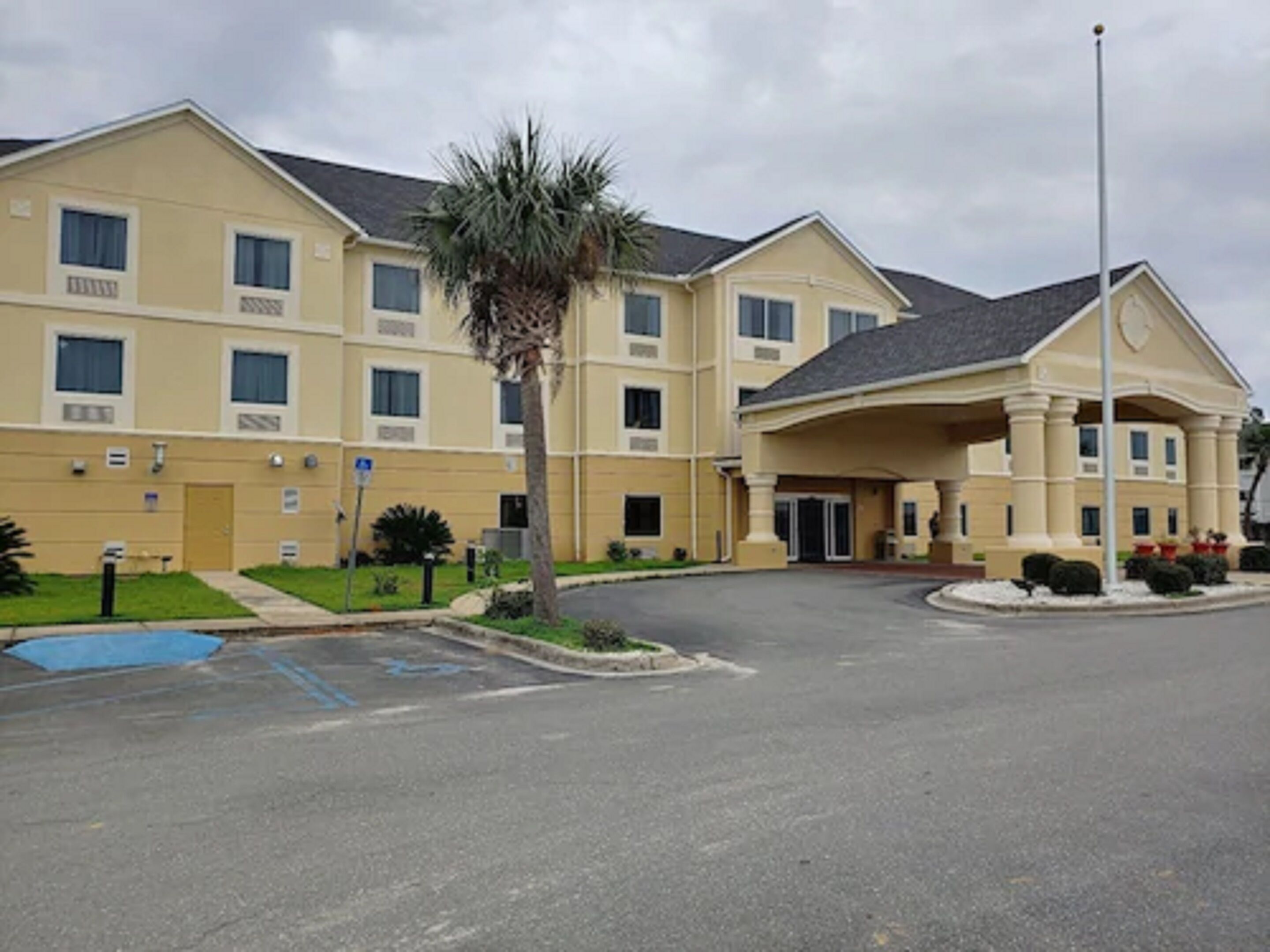 A multi-story hotel with a central entrance, a parking lot, and a palm tree.