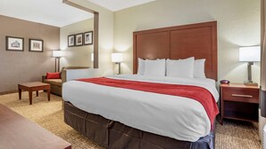 Una habitación de hotel con una cama grande, un sofá, una mesita pequeña y una mesita de noche con lámpara.