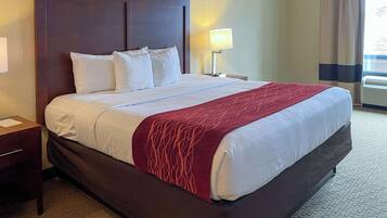 A hotel room with a large bed, a nightstand, a lamp, and a window with curtains.