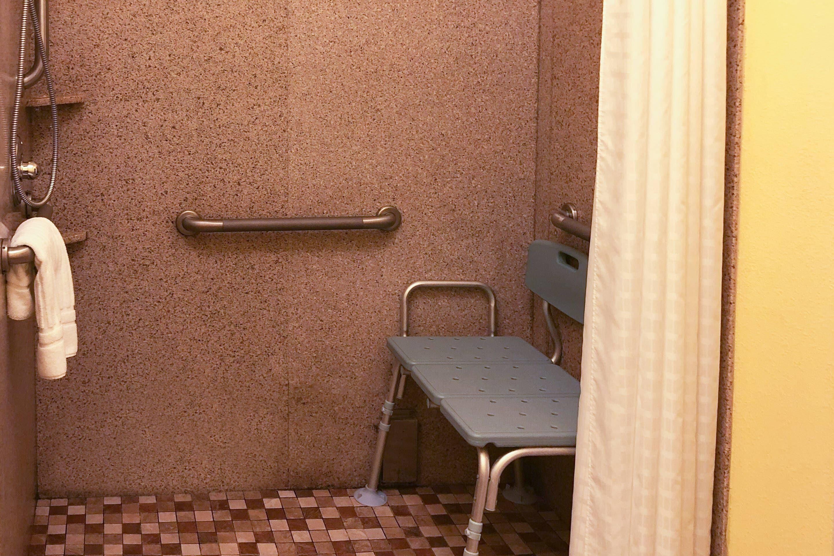 A bathroom with a textured wall, a grab bar, a wheelchair-accessible bench, and a tiled floor.
