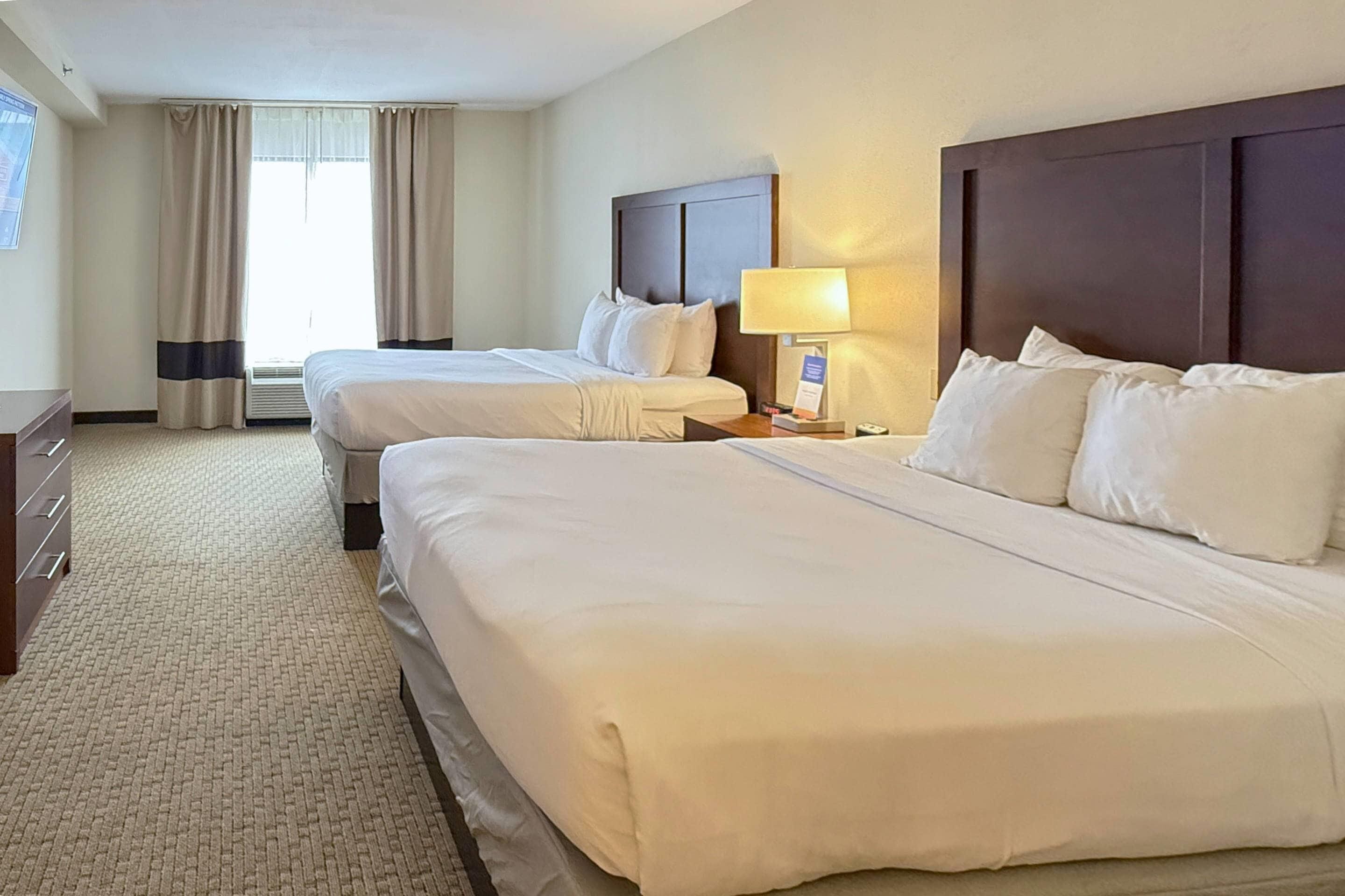 Habitació d'hotel amb dos llits, un escriptori, una làmpada i una finestra amb cortines.