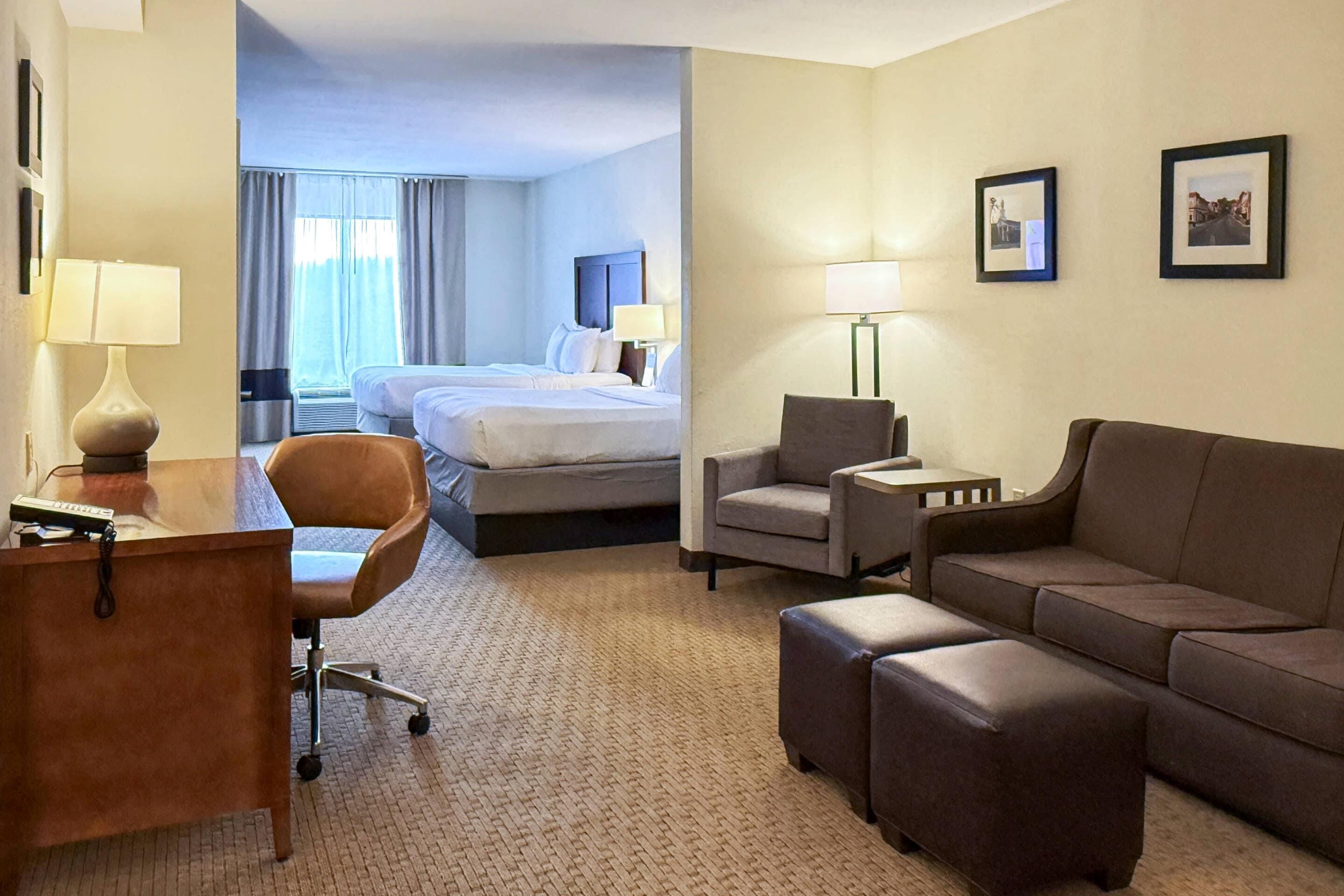 A hotel room with a desk, two chairs, a sofa, a bed, and a small table with a lamp.