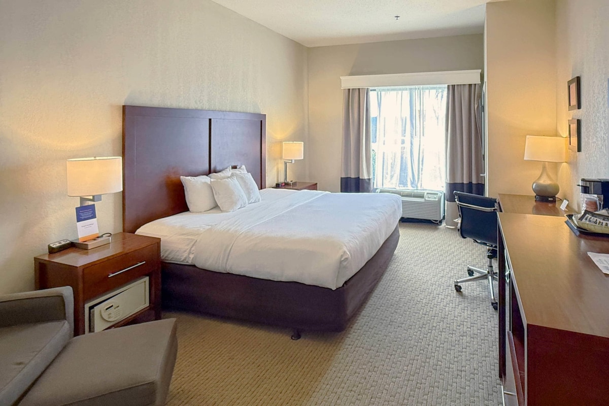 A hotel room with a large bed, bedside tables with lamps, a desk with a chair, and a window with curtains.