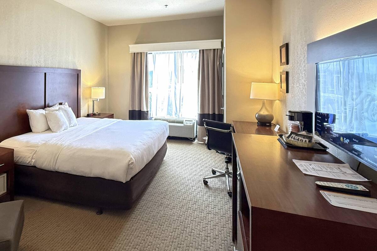 A hotel room with a large bed, a desk with a computer, a TV, and a window with curtains.