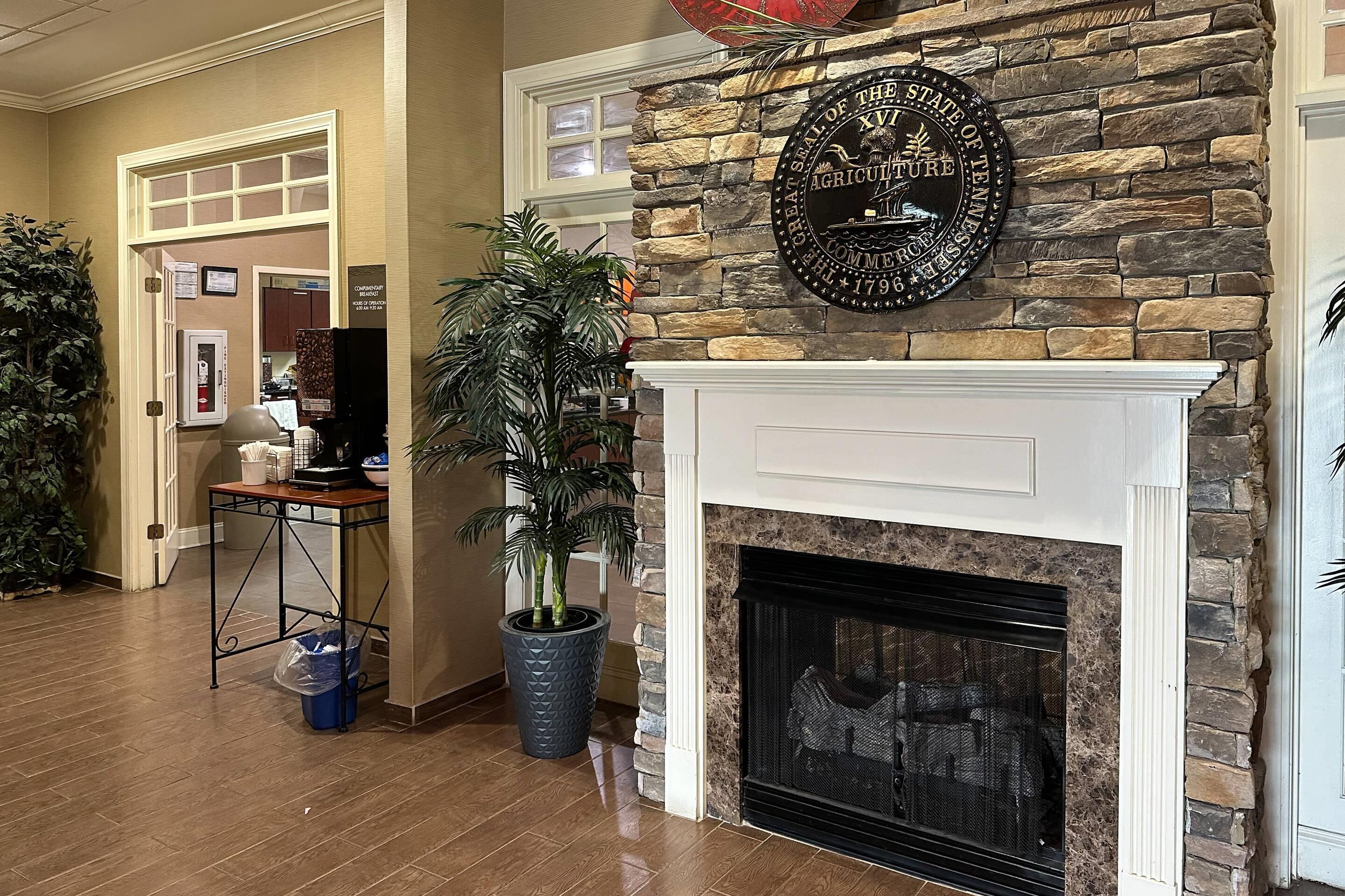 A room with a stone fireplace, a mounted sign, a potted plant, and a trash bin.