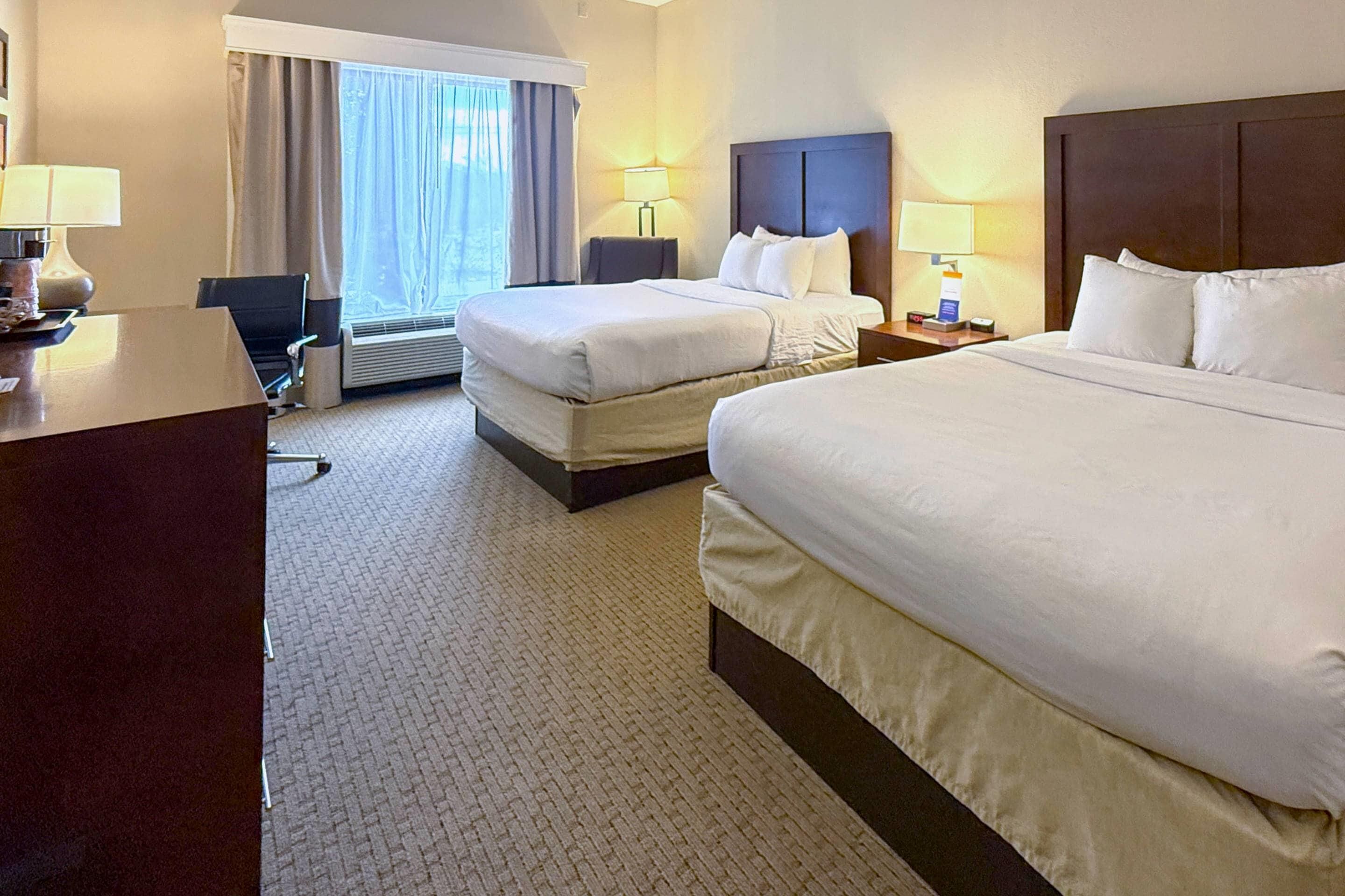 Ein Hotelzimmer mit zwei Betten, einem Schreibtisch, einem Stuhl und einem Fenster mit Vorhängen.