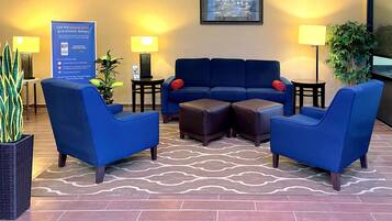 Un hall d’entrée avec un canapé bleu, deux fauteuils, une petite table et une plante en pot.