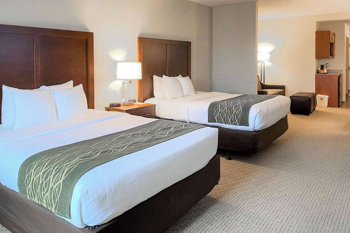 Une chambre d’hôtel avec deux lits, un bureau, une chaise, une lampe et une petite kitchenette.