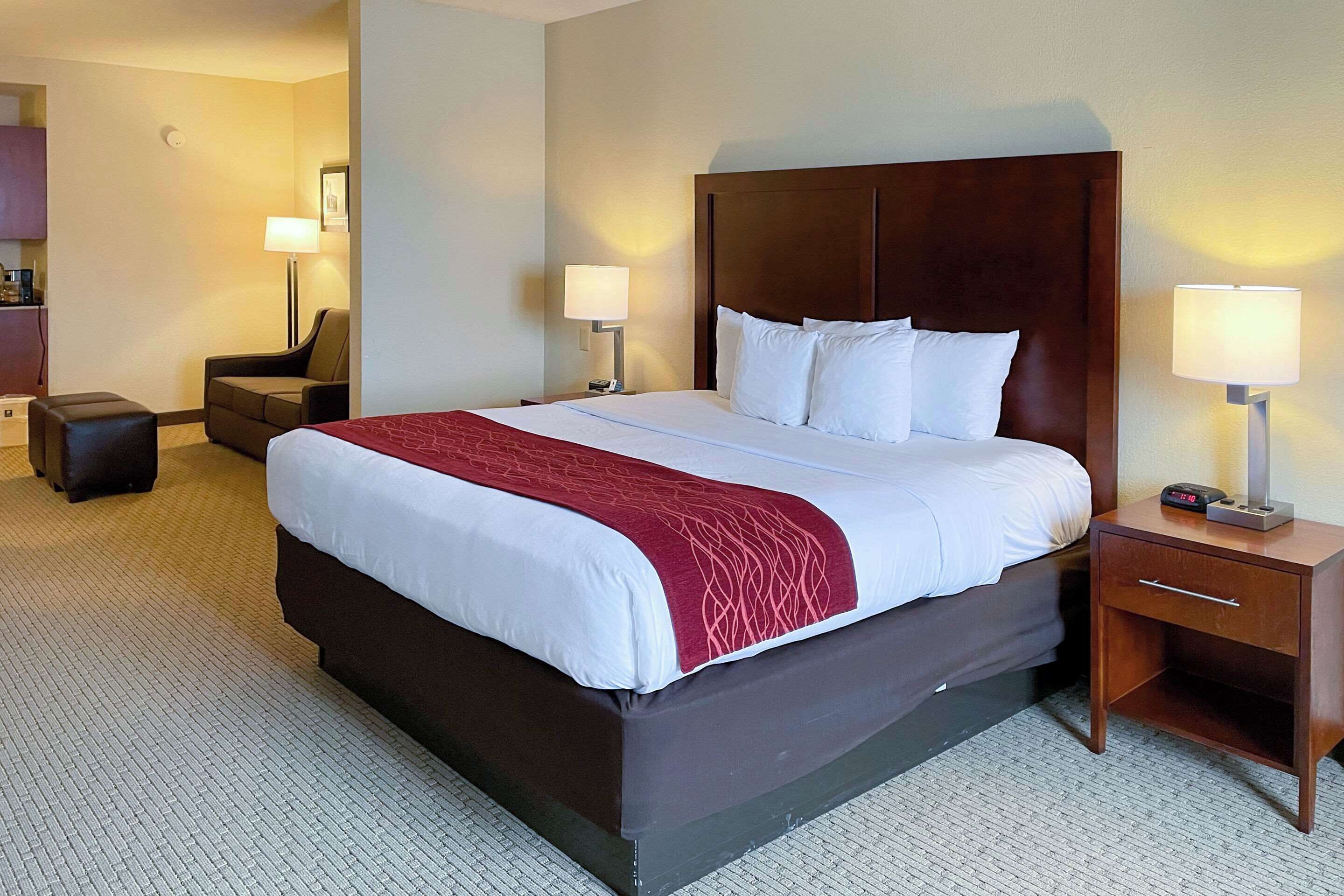 A hotel room with a large bed, a nightstand with a lamp, a chair, and a small table.