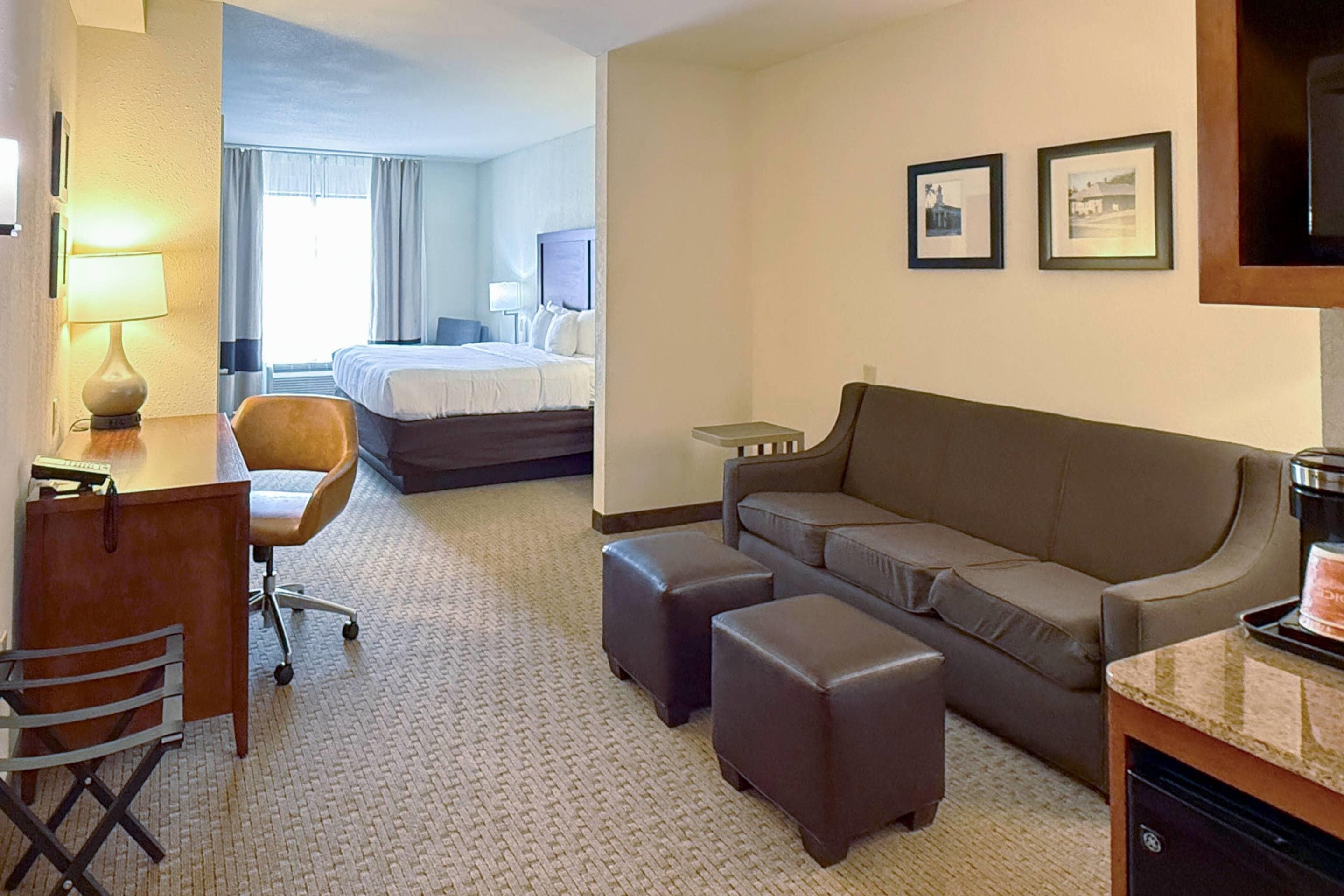 A hotel room with a desk, chair, sofa, ottoman, and a bed.