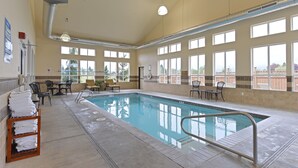 Una piscina interna con pavimento piastrellato, una scaletta e diversi lettini e tavolini intorno all'area piscina.