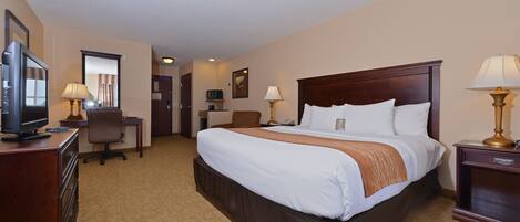 A hotel room with a large bed, a desk with a chair, a television, and two bedside lamps.