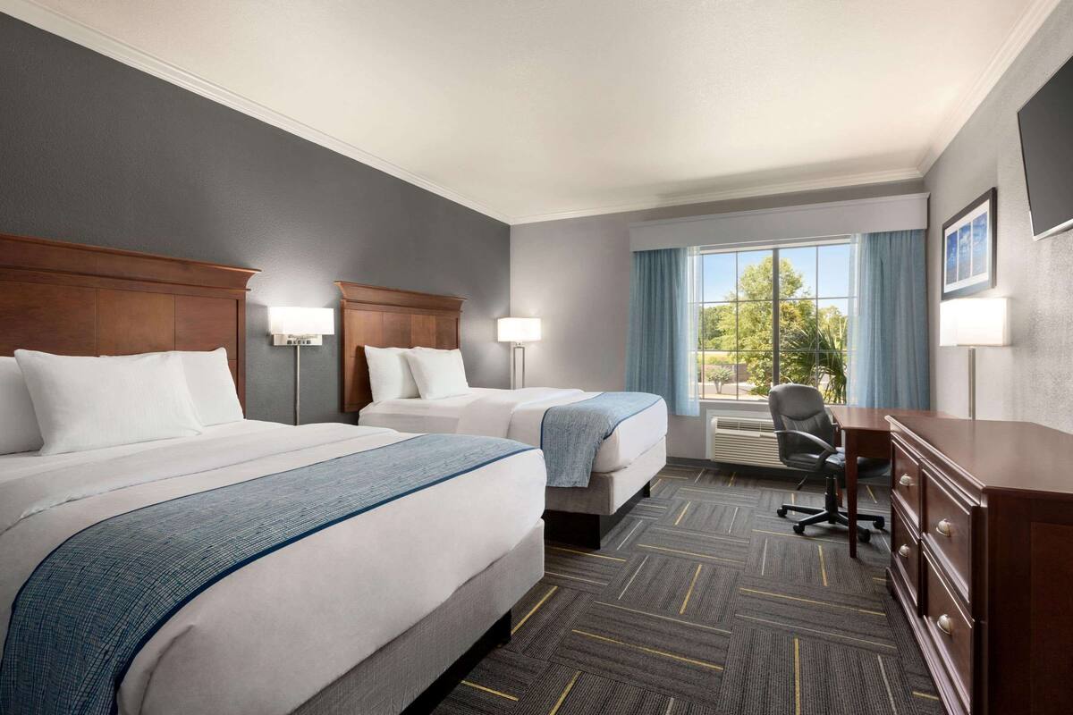 A hotel room with two beds, a desk, a chair, and a dresser.