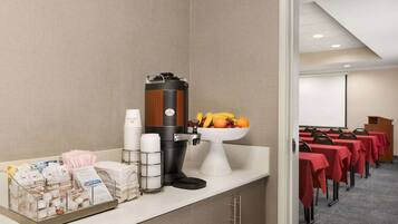 A hotel room with a kitchenette, a coffee machine, a fruit bowl, and a conference room with red tablecloths.