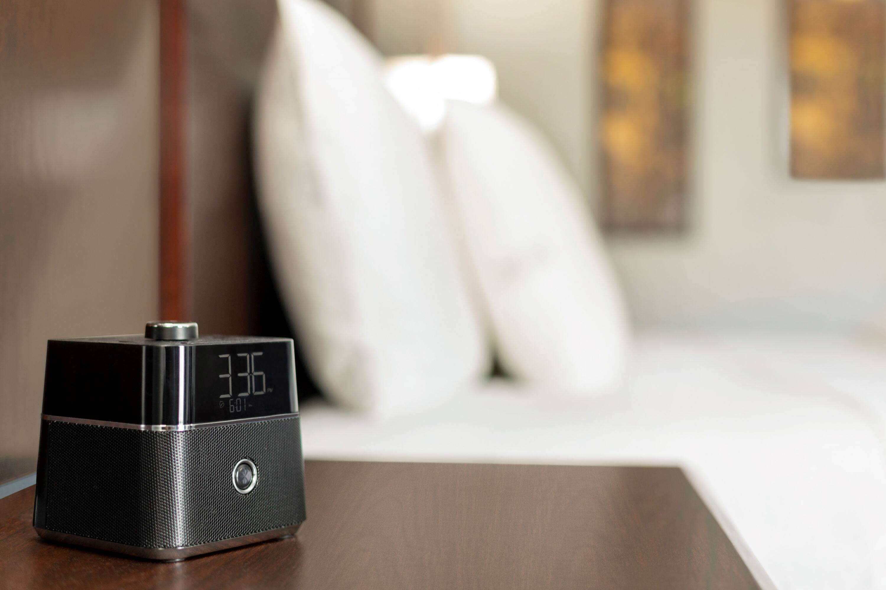 A digital clock on a bedside table in a hotel room.