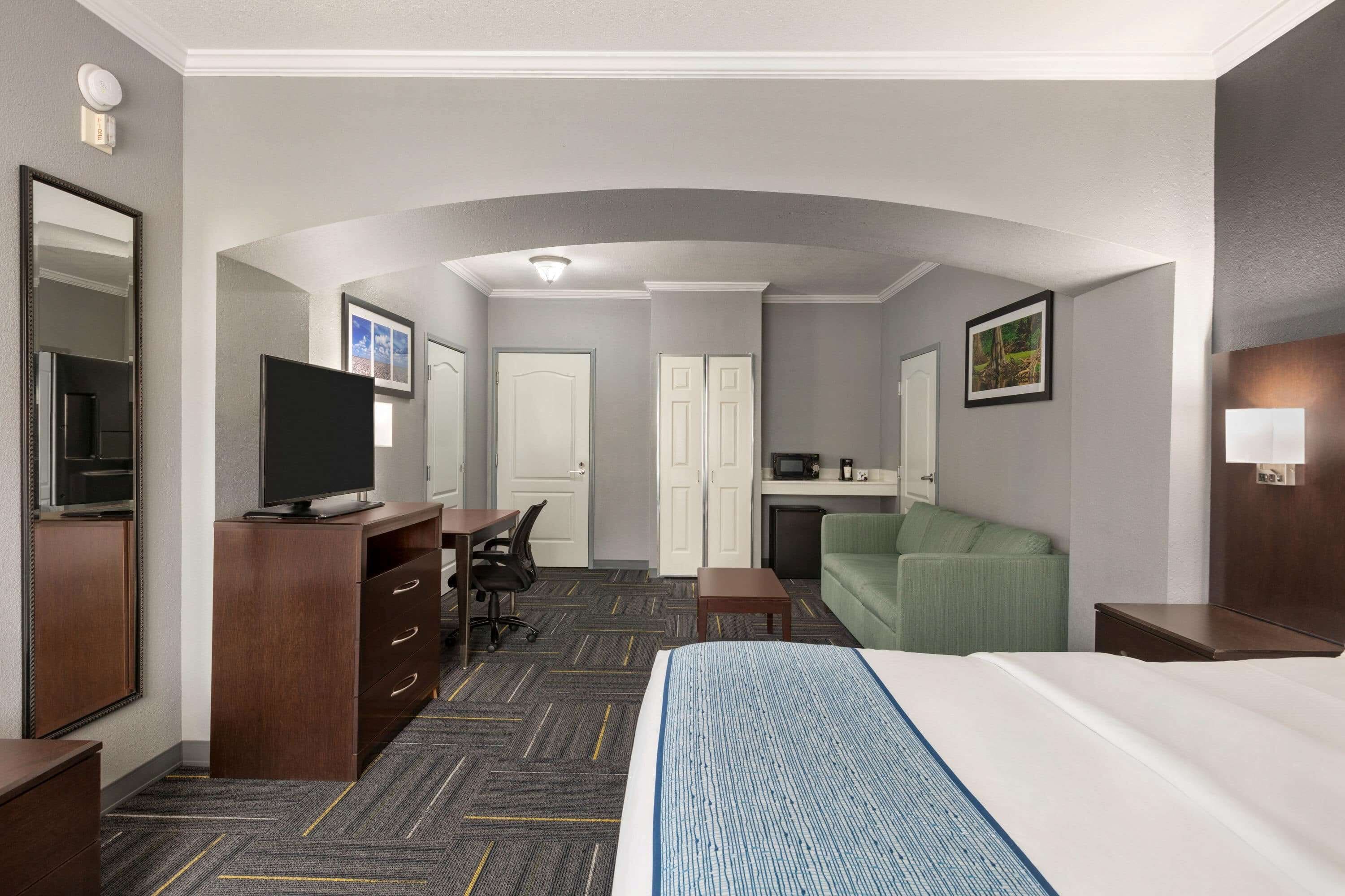 A hotel room with a bed, a desk, a television, a green sofa, and a microwave.