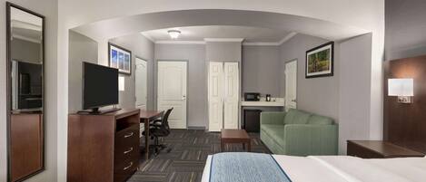 A hotel room with a bed, a desk, a television, a green sofa, and a microwave.