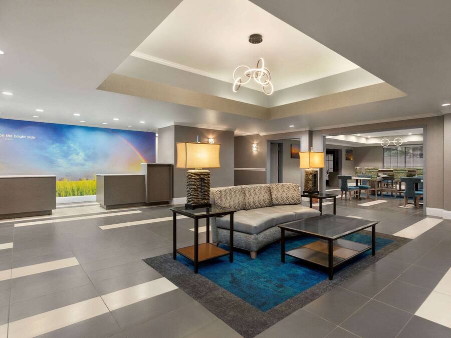A modern lobby with a sofa, coffee table, and lamps. There is a reception desk and a dining area in the background.