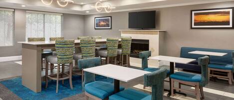 A hotel lobby with a bar area, seating arrangements, a fireplace, and a television mounted on the wall.
