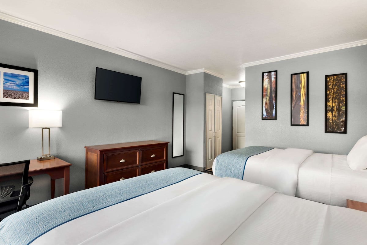 A hotel room with two beds, a desk, a chair, a dresser, a flat-screen TV, and framed pictures on the wall.
