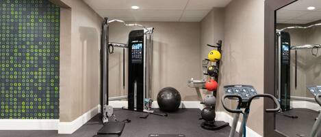 Un gimnasio con equipamiento de ejercicio, un espejo grande y un muro con diseño.
