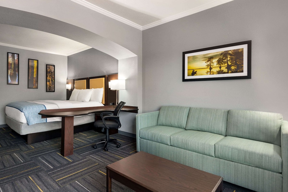 A hotel room with a bed, a green sofa, a wooden table, and a desk with a lamp.