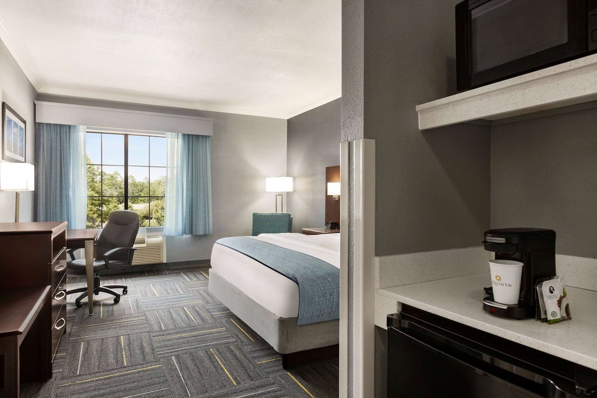 A hotel room with a bed, desk, chair, and a coffee maker.