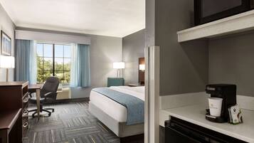 A hotel room with a bed, desk, chair, and a coffee maker.