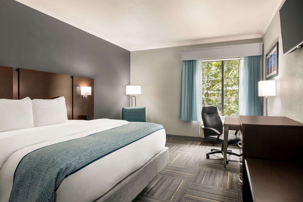 A hotel room with a large bed, a desk, a chair, and a window with curtains.