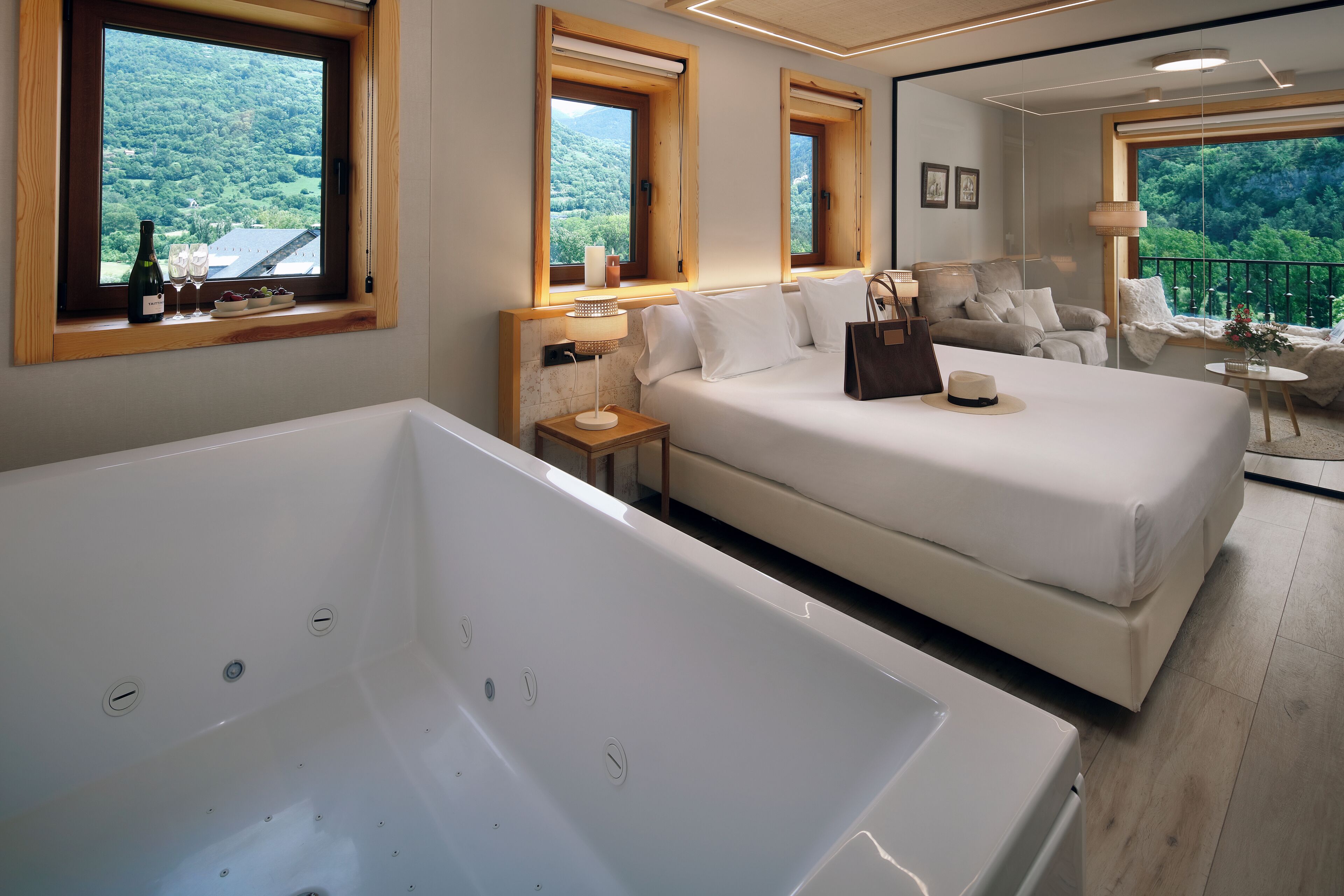 Un dormitorio moderno con una bañera grande, una cama doble, un sofá y un balcón con vistas al bosque.