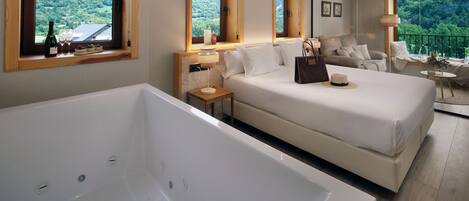 Un dormitorio moderno con una bañera grande, una cama doble, un sofá y un balcón con vistas al bosque.