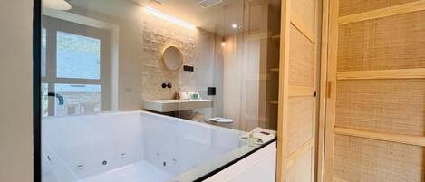 Un baño moderno con una bañera grande, un espejo redondo y una puerta corredera de madera.